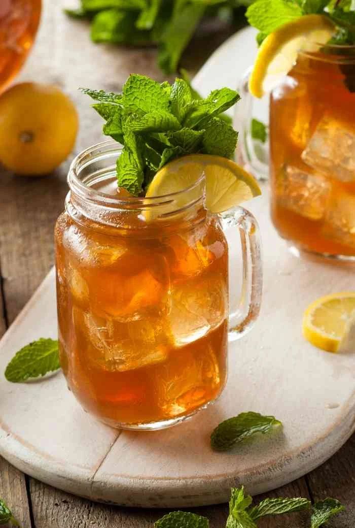 two mason jars filled with lemonade and mint tea on a white tray surrounded by limes