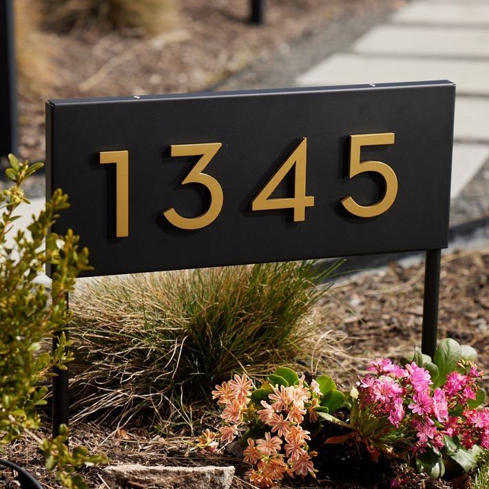 a black and gold house number sign next to flowers