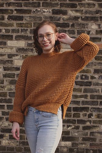 a woman wearing glasses standing in front of a brick wall with her hand on her head