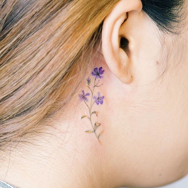 a woman's ear with small purple flowers on the back of her left ear