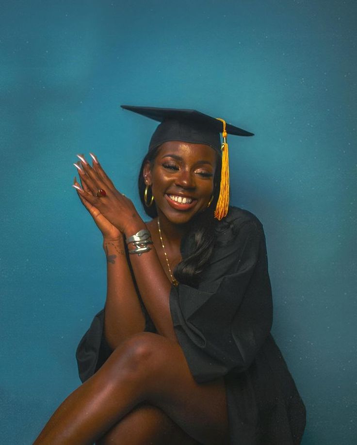 a woman in a graduation cap and gown sitting on the ground with her legs crossed