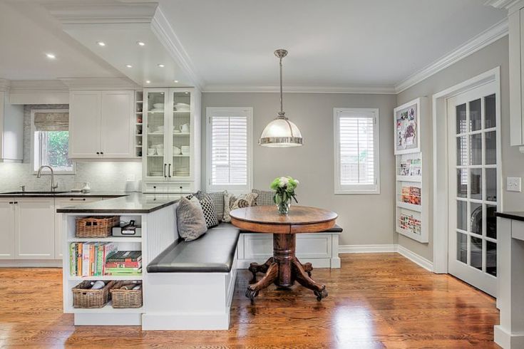 a kitchen with white cabinets and wood floors, along with a breakfast nook in the center