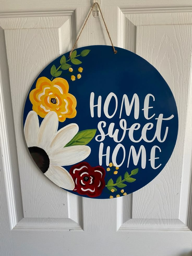 a blue sign that says home sweet home with flowers on it hanging from the front door