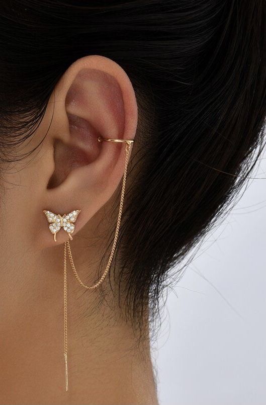 a close up of a person's ear with a butterfly on the chain attached to it