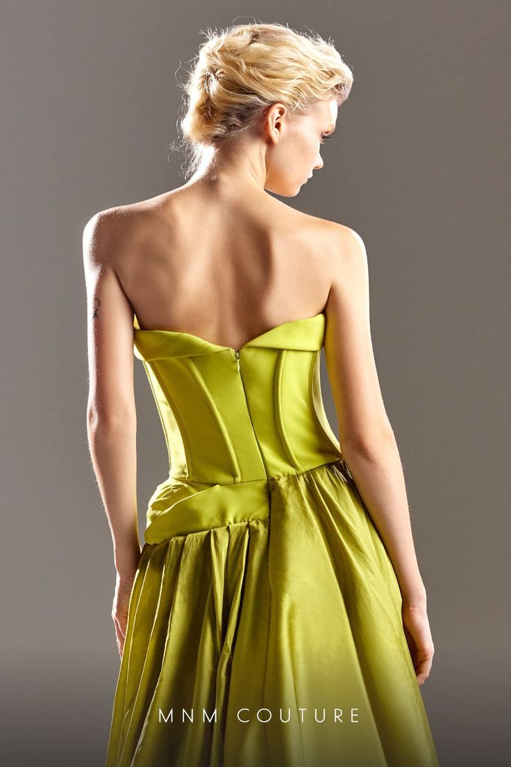 the back of a woman in a green dress with her hand on her hip, looking down