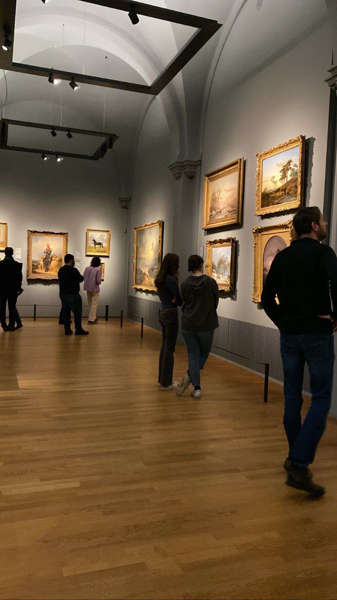 people are looking at paintings in an art gallery with wooden floors and ceilings, while others look on