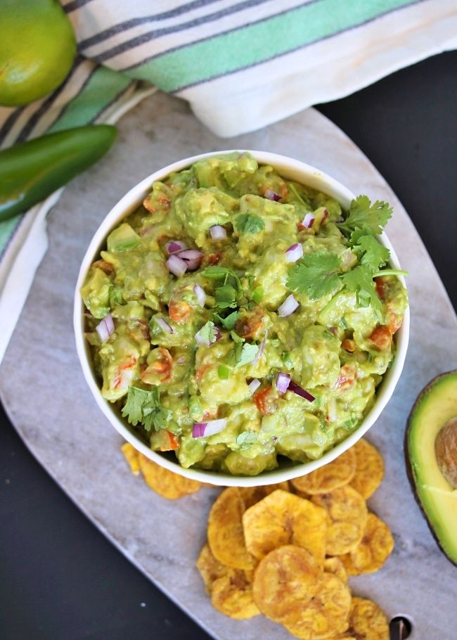 a bowl of guacamole next to chips and an avocado