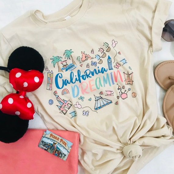 a white shirt with the words california dreaming on it and minnie mouse ears next to some other items