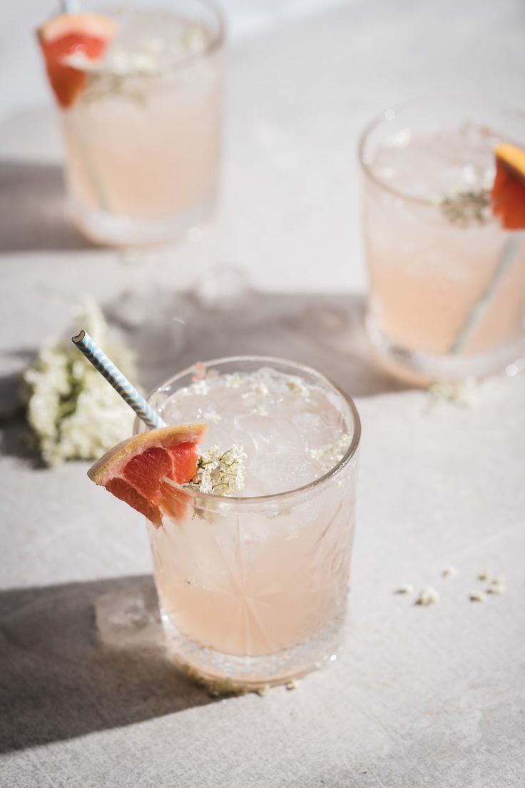 two glasses filled with drinks and garnished with grapefruit on the side