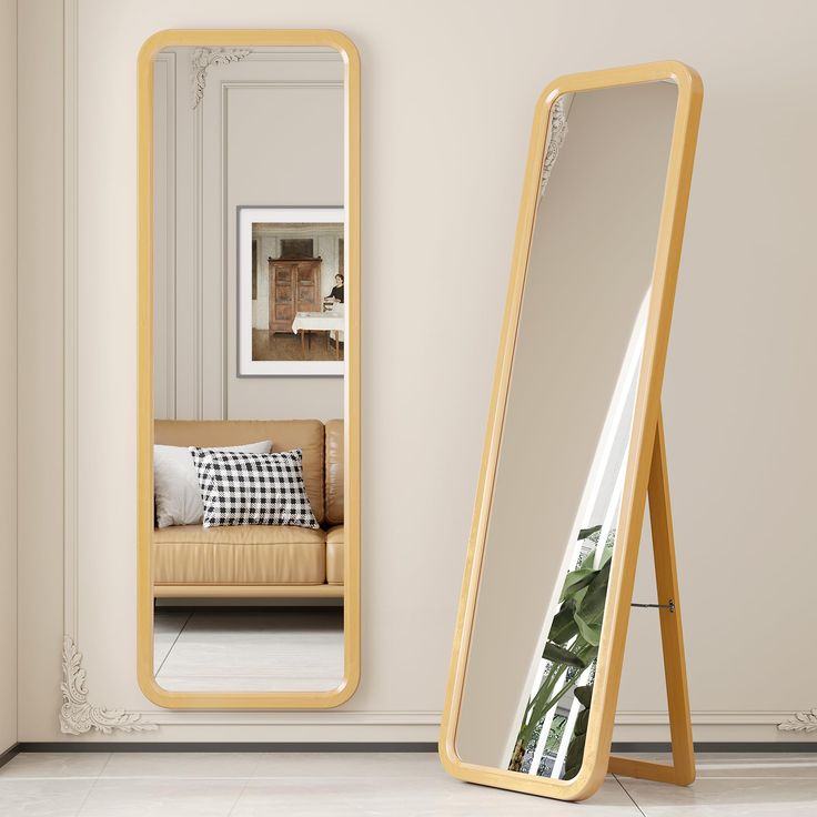 a large mirror sitting next to a couch on top of a tiled floor in front of a white wall