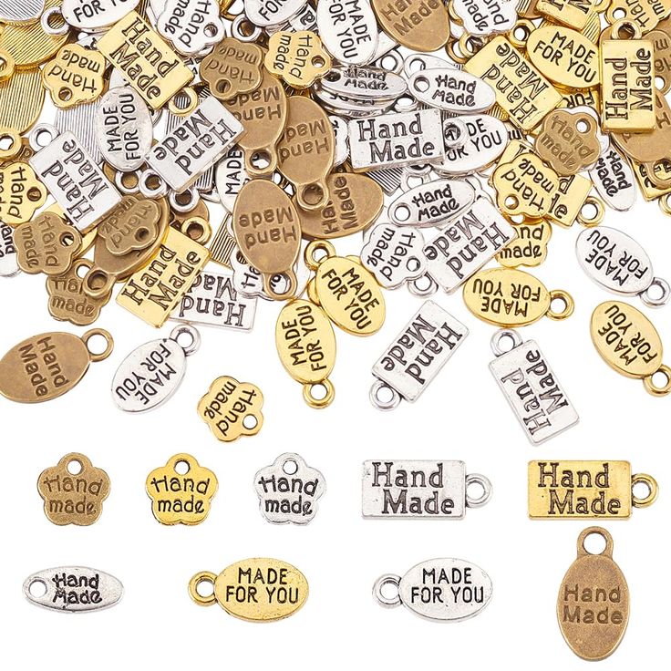 lots of gold and silver metal charms with words on them that say, hand made