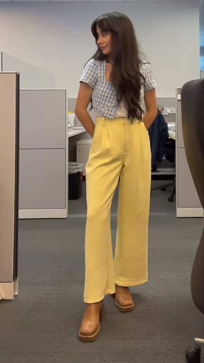 Girl with long brown hair stands in office with a blue gingham short sleeved cardigan, with a white cami underneath, yellow pants, and beige boots. Pink And Green Work Outfit, Color Business Outfits, Office Cool Girl Outfit, Cute Office Wear, Business Casual Fun Outfit, Office Friendly Outfits, Fun Office Wear, Pastel Corporate Outfit, Unique Business Casual Outfits For Women