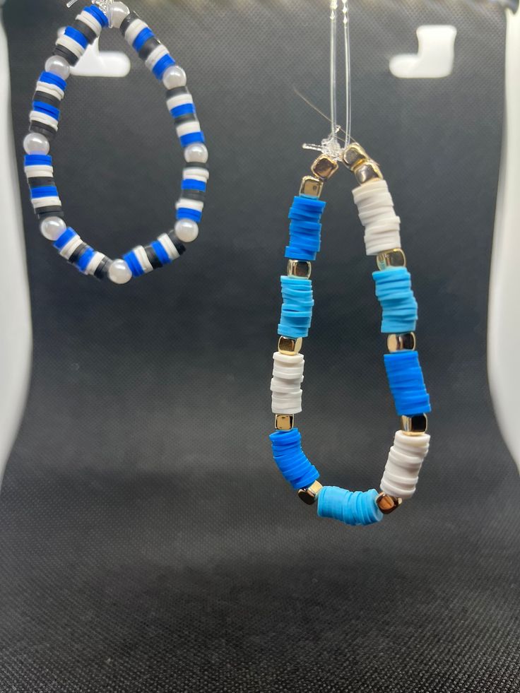 two blue and white beaded earrings hanging from a hook in front of a gray background