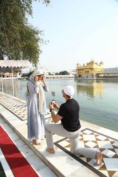 a man kneeling down next to a woman in front of a body of water while taking a picture