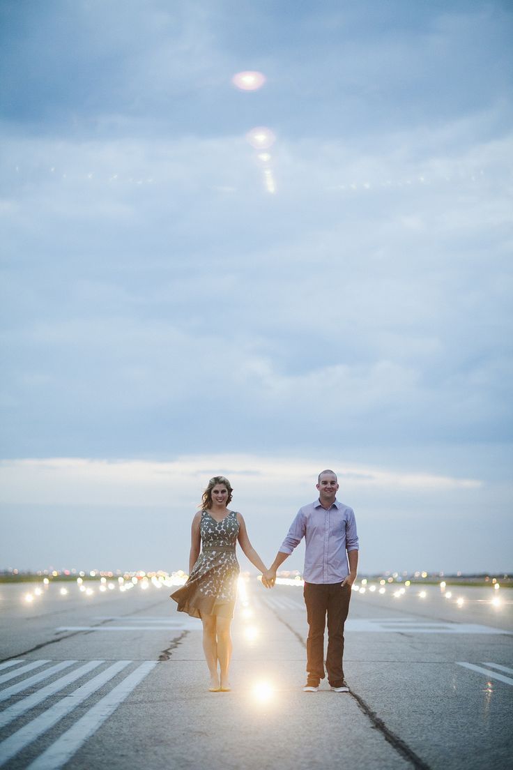 a man and woman holding hands walking across an airport tarmac