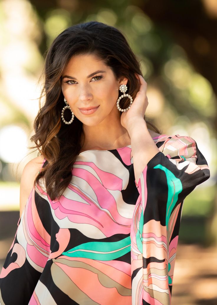 a beautiful woman in a colorful dress holding her hand on her head and looking at the camera