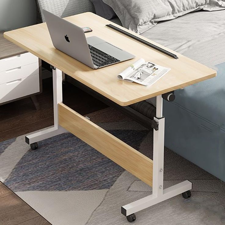 a laptop computer sitting on top of a wooden desk next to a bed with pillows