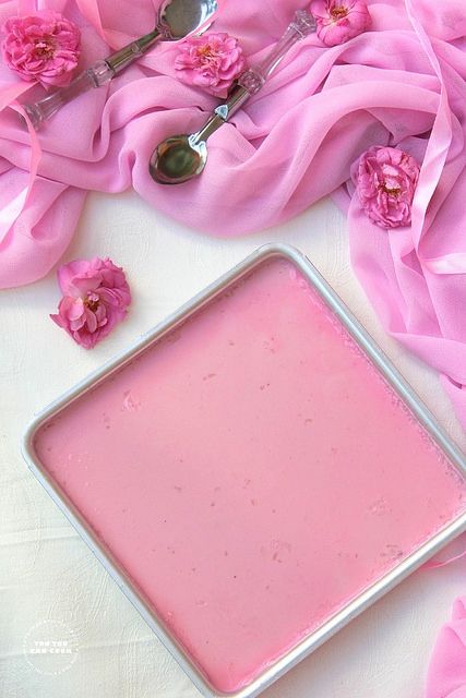 a pink substance in a metal pan on a white table cloth with spoons next to it