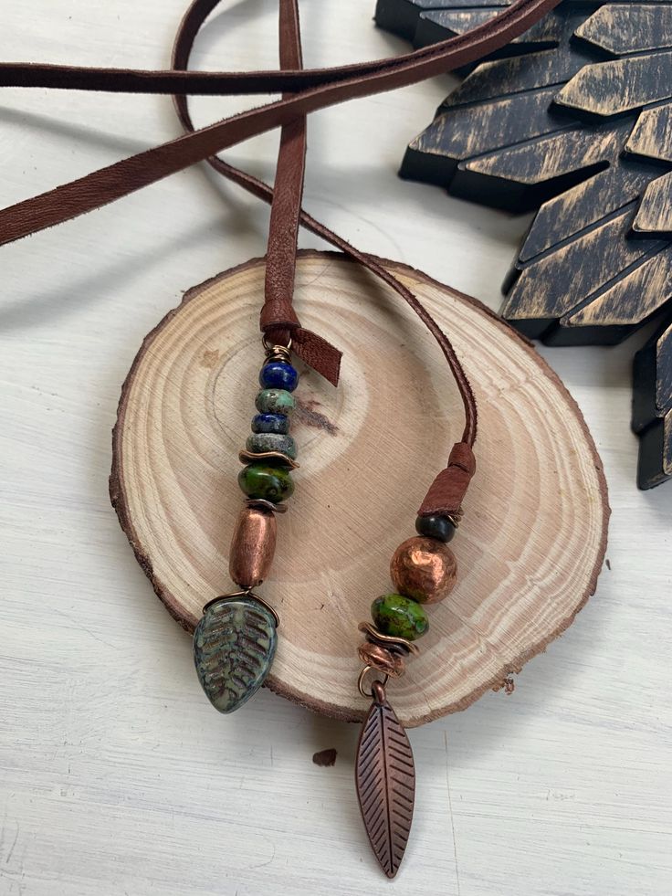 a necklace with leaves and beads hanging on a piece of wood next to a tree branch