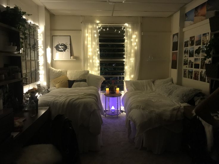 two beds in a room with lights on the wall and windows behind them, all white