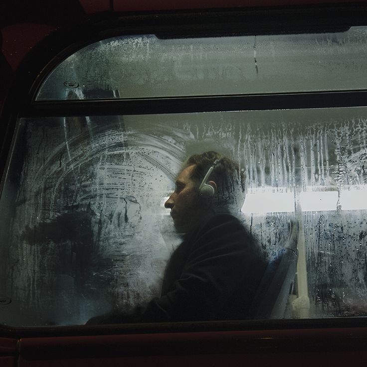 a man sitting on a bus with headphones in his ears looking out the window