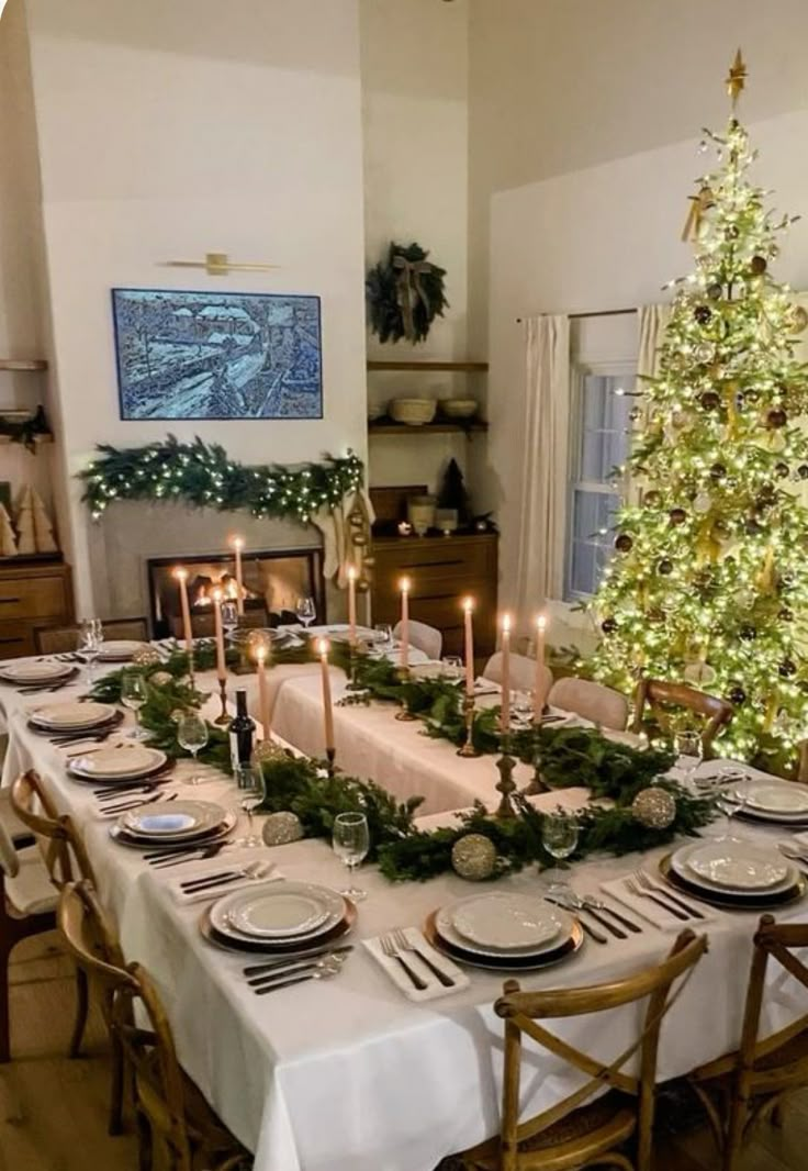 a dining room table set for christmas dinner with candles and greenery on the table