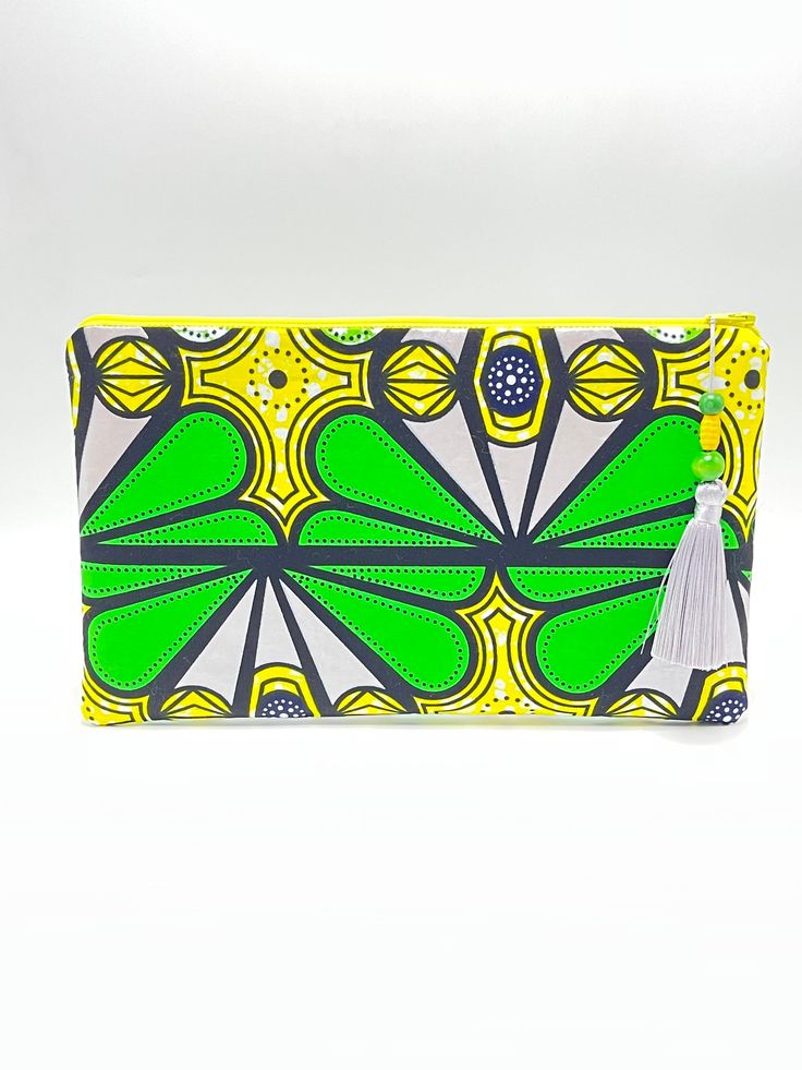 This beautiful graphic pattern clutch is great for the spring & summer seasons!  The beautiful green, yellow, silver, white, and black pattern makes a statement!  It measures 12 inch Width X 7 1/2 inch Length perfect for your essentials and more.  It has a yellow zipper for closure adorned with a silver gray 3 1/2 inch tassel adorned with green and yellow wooden beads.  The inside is lined in green along with an inside pocket. Trendy Green Clutch Pouch, Trendy Green Rectangular Clutch, Green Pouch Clutch For Summer, Trendy Green Pouch Clutch, Trendy Green Clutch As A Gift, Green Clutch For Everyday Use In Summer, Trendy Green Clutch As Gift, Trendy Green Clutch For Gift, Yellow Rectangular Clutch For Summer