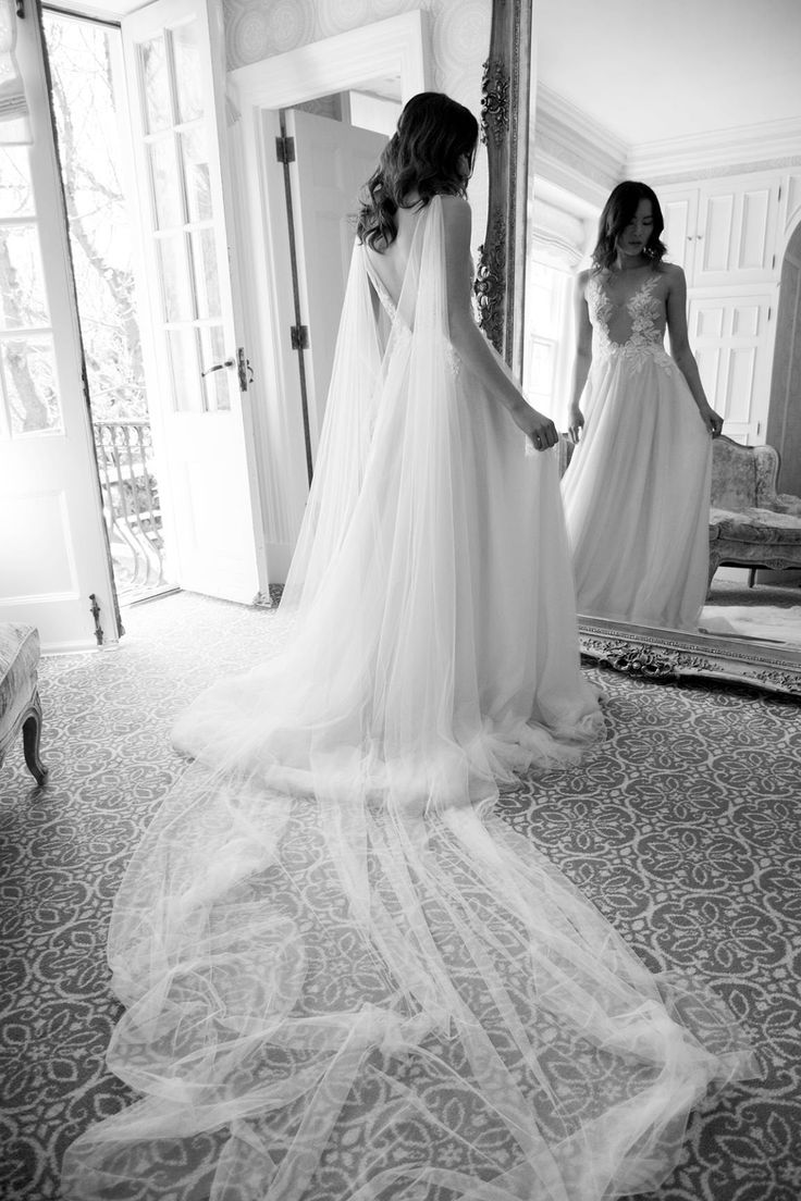 two women standing in front of a mirror wearing wedding gowns and veils on their heads