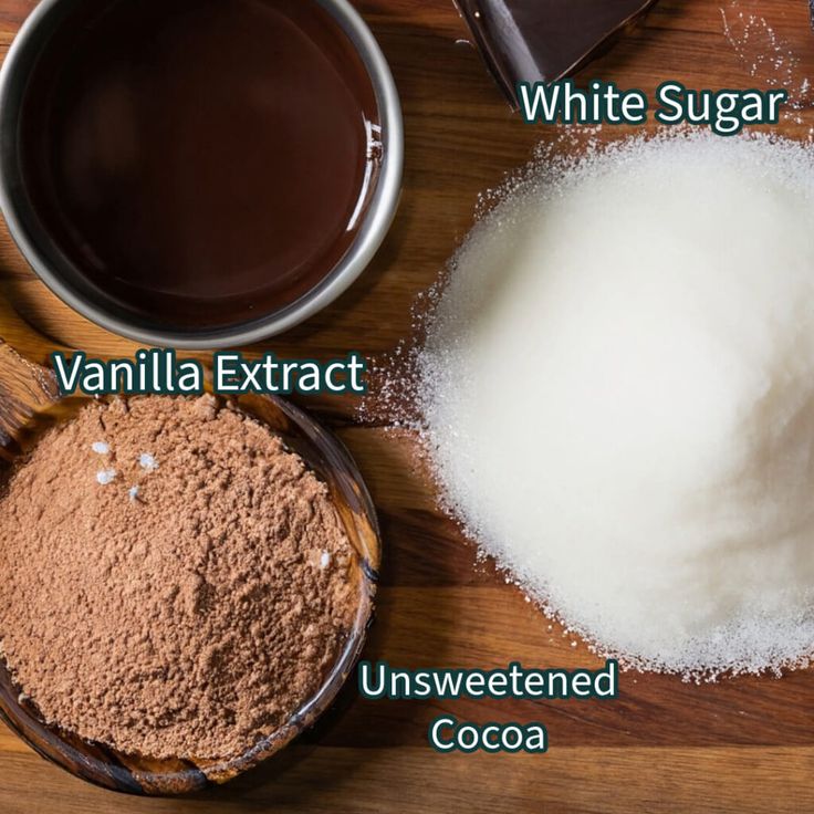 ingredients to make chocolate cake sitting on a wooden table with white sugar, vanilla extract and unsweeted cocoa