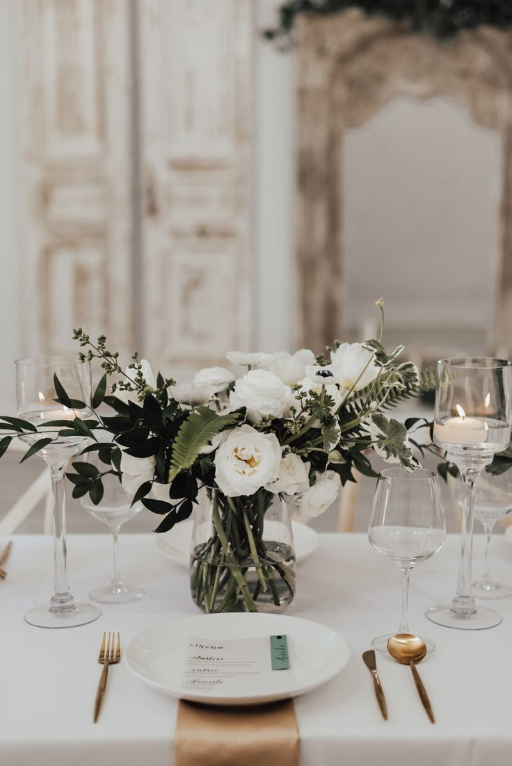 the table is set with white flowers and gold place settings for an elegant wedding reception