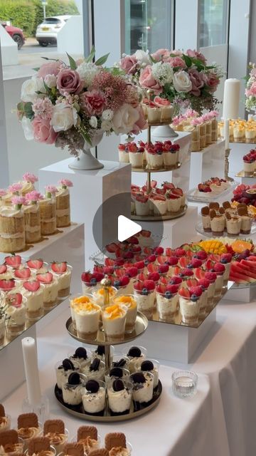 a table topped with lots of desserts and flowers on top of white cloth covered tables