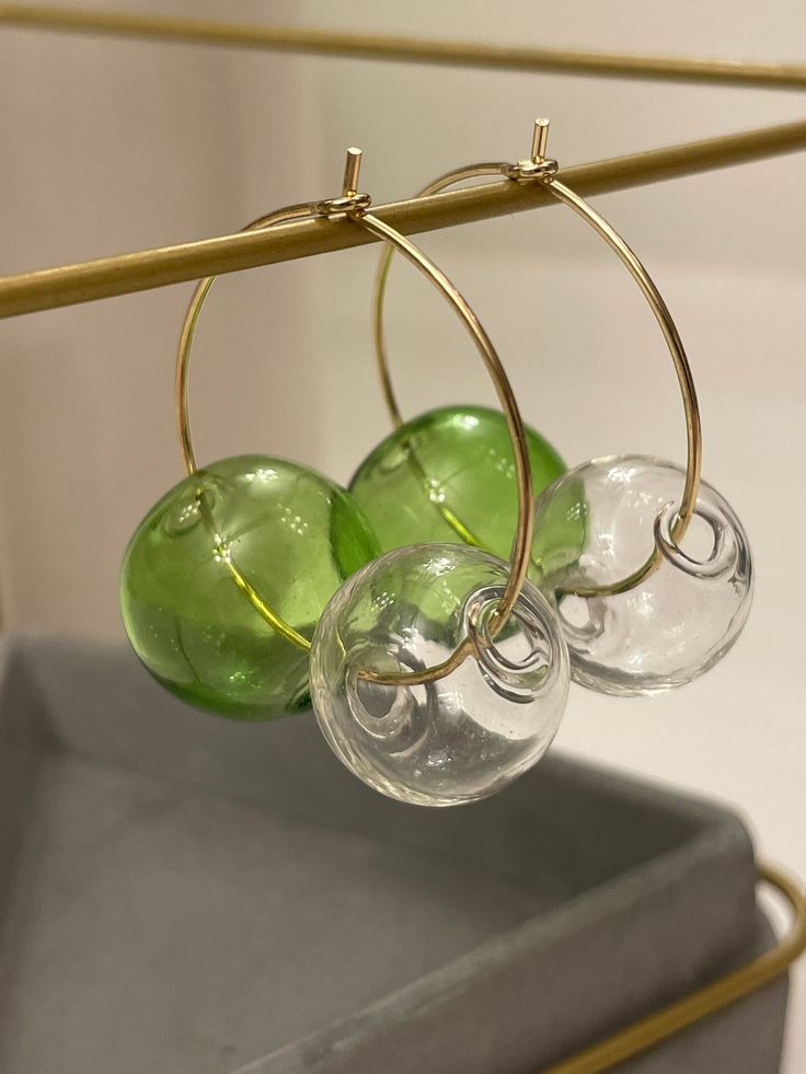 three wine glasses are hanging from a metal rack with gold hoops and green glass beads