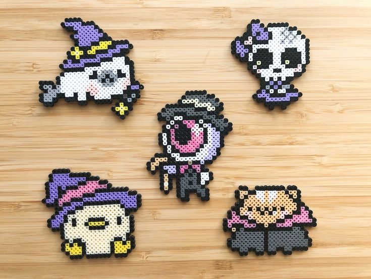 four pixel art magnets on a wooden surface with one being a witch and the other is a cat