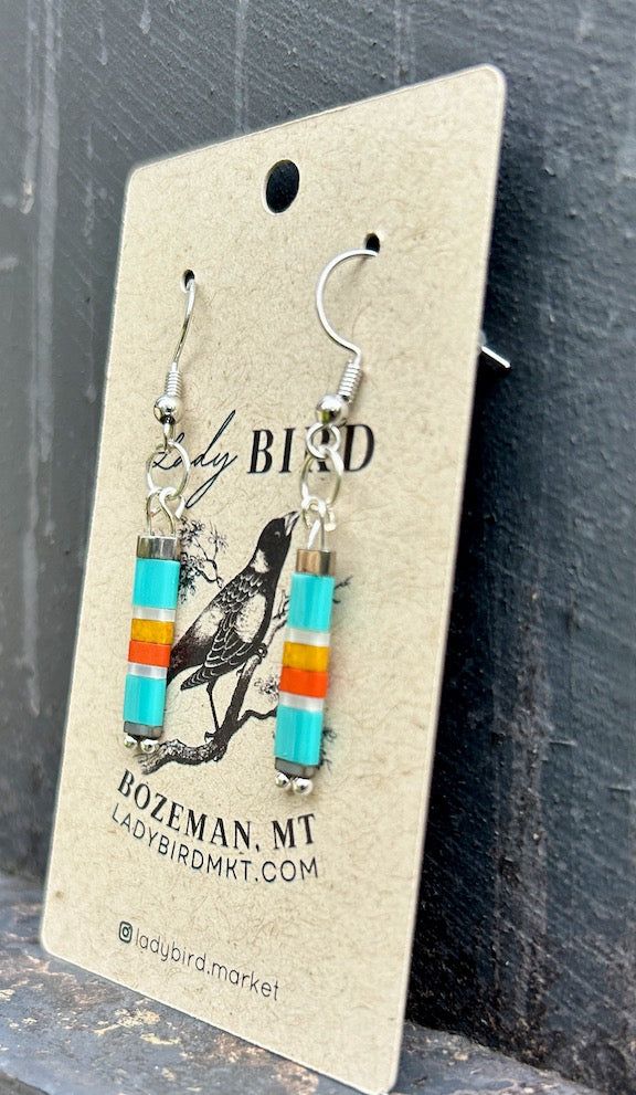 Featuring a throwback retro-style color combo, turquoise blue with orange, yellow, and silver or gold stripes (depending on your preference), these beaded dangle earrings are classy yet playful, with a tinge of boho style, designed to make you and your outfit happy. Pair it with the Retro-Style Tila Bracelets for the win! Our Tila Bead Collection includes a variety of handmade earrings and stretchy bracelets made with Japanese glass Miyuki Tila Beads, known for their quality, durability, and bea Retro Beaded Jewelry For Gifts, Retro Beaded Jewelry As Gift, Retro Beaded Jewelry Gift, Retro Beaded Dangle Jewelry, Adjustable Retro Drop Earrings, Retro Adjustable Drop Earrings, Retro Blue Drop Earrings, Blue Southwestern Style Earrings For Gift, Tila Bead Jewelry