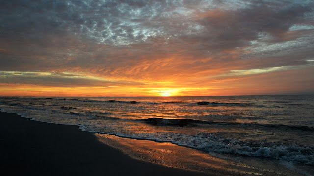 the sun is setting over the ocean with waves coming in