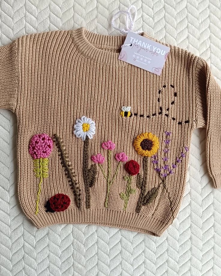 a knitted sweater with flowers on the front and back is sitting on a bed