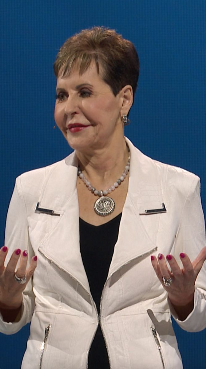 a woman standing in front of a blue background wearing a white jacket and black top