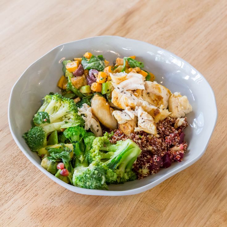 a white bowl filled with broccoli, meat and other vegetables on top of a wooden table