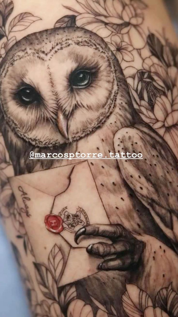 an owl tattoo on the arm with flowers around it and a letter in its hand