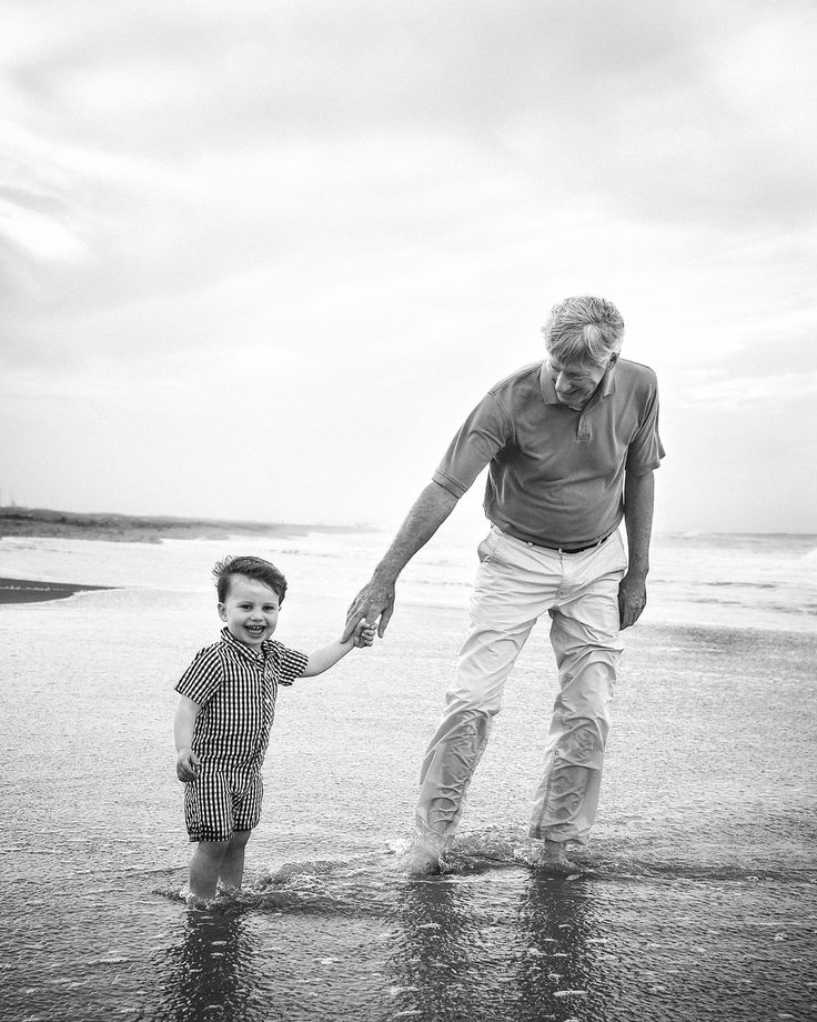 an older man holding the hand of a small child on a beach near the ocean