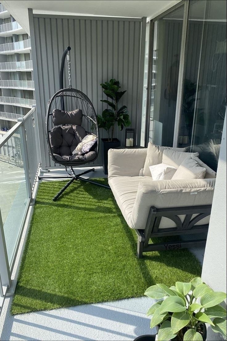 a balcony with a swing chair, couch and potted plant on the grass area