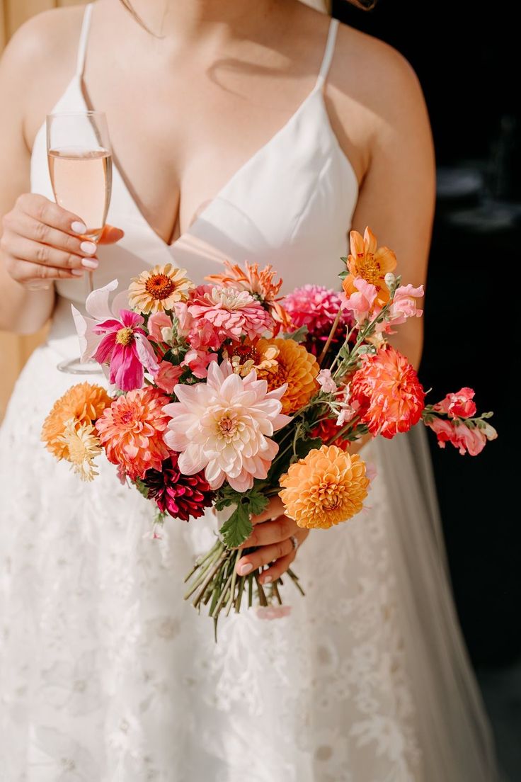 a woman in a white dress holding a bouquet of flowers and a glass of wine