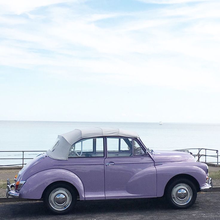 an old purple car parked in front of the ocean