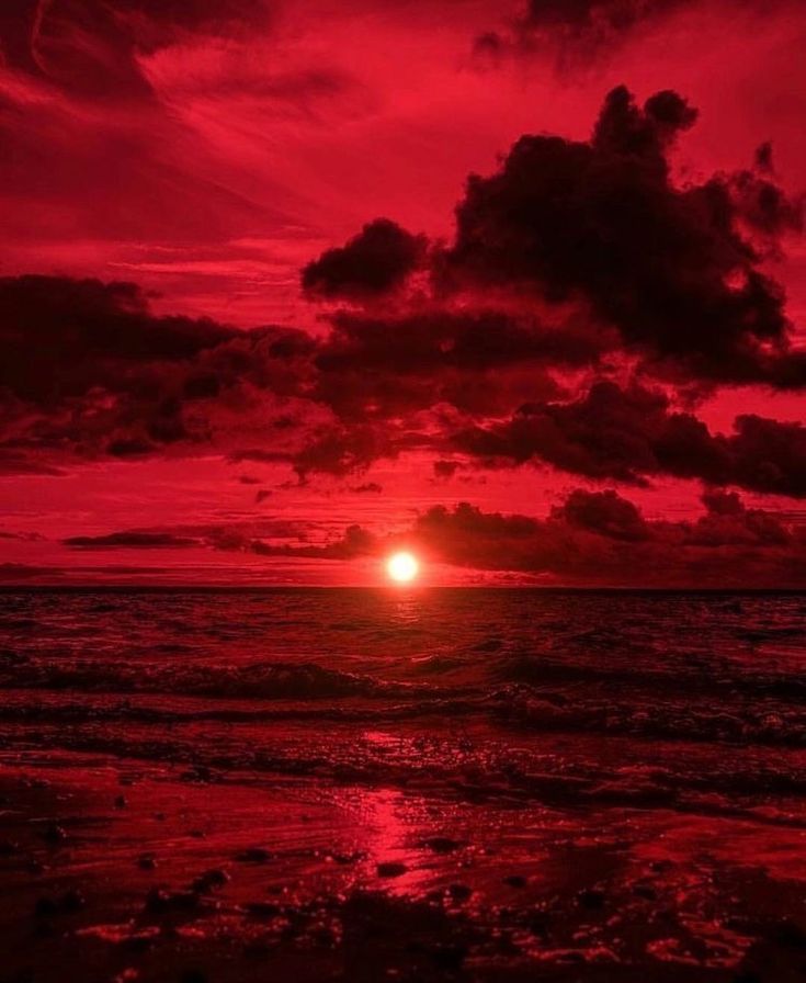 the sun is setting over the ocean with clouds in red and black colors on it