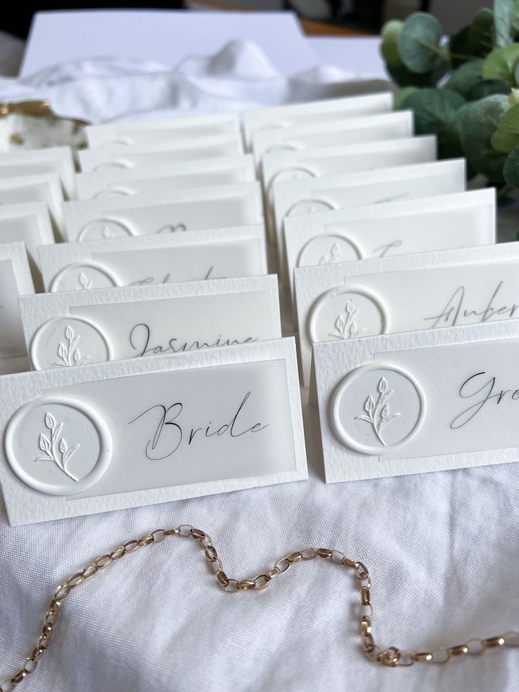 wedding place cards are laid out on a white tablecloth with flowers in the background