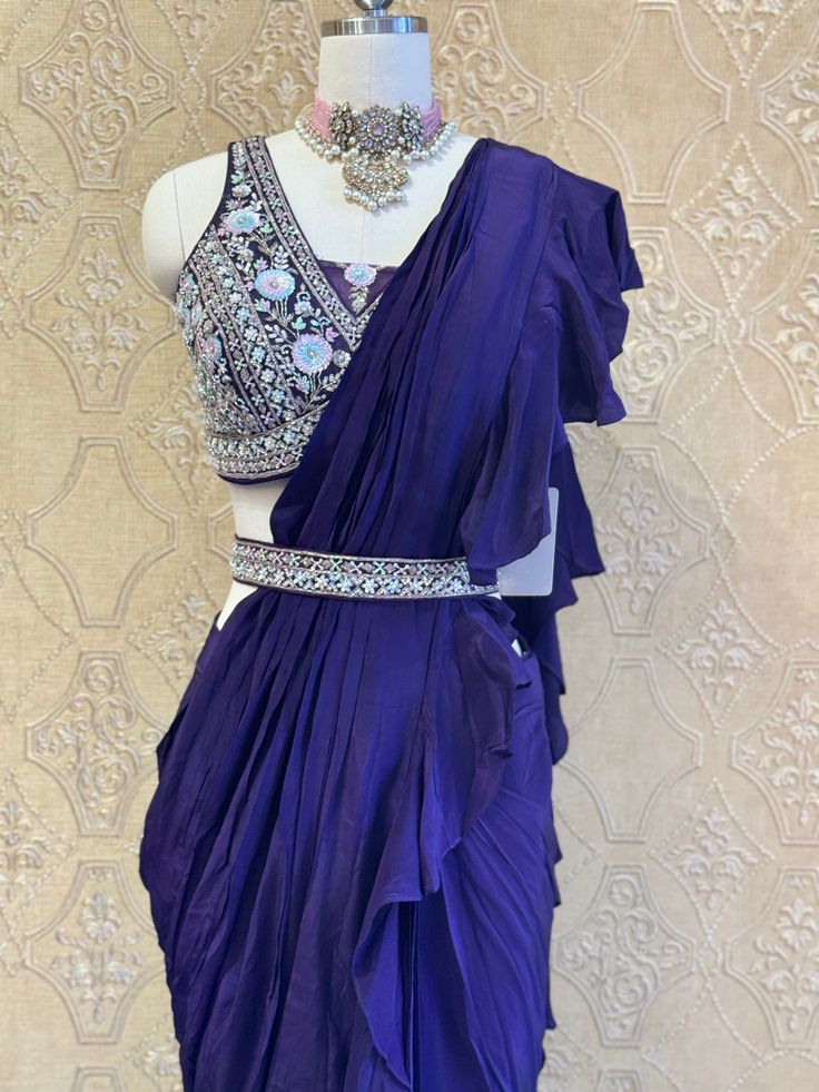 This deep purple ruffled saree exudes elegance with its cascading layers, paired with a heavily embellished blouse and a matching belt. Perfect for weddings and festive occasions, it blends traditional charm with a modern touch. Key Features: Color: Deep Purple Design: Ruffled saree with a fully hand-embellished blouse Accessories: Matching belt for a defined silhouette Occasion: Ideal for weddings, festive events, and grand celebrations Designer Wear Saree With Ruffles In Traditional Drape, Traditional Designer Choli With Ruffles, Traditional Ruffled Choli For Designer Wear, Bollywood Style Purple Pre-draped Saree For Wedding, Traditional Drape Wedding Wear With Ruffles, Purple Embellished Pre-draped Saree, Traditional Wedding Wear With Ruffles And Traditional Drape, Embellished Purple Pre-draped Saree, Elegant Purple Pre-draped Saree