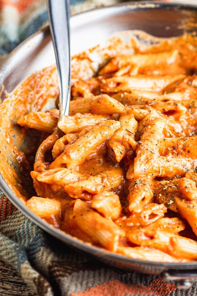 a bowl filled with pasta and sauce on top of a tablecloth next to a fork