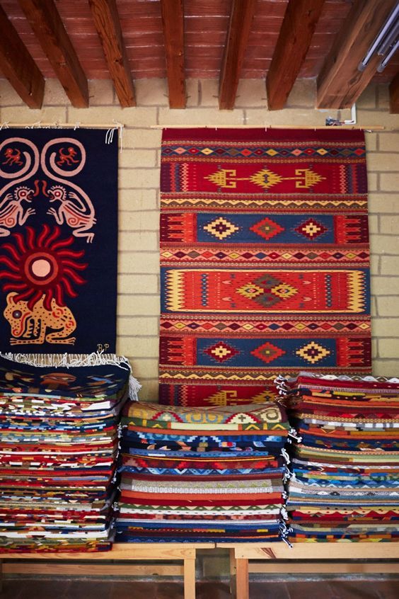 several colorful rugs are on display in a room with wooden beams and brick walls