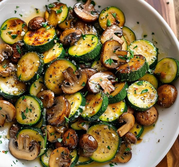 a white bowl filled with mushrooms and zucchini on top of a wooden table