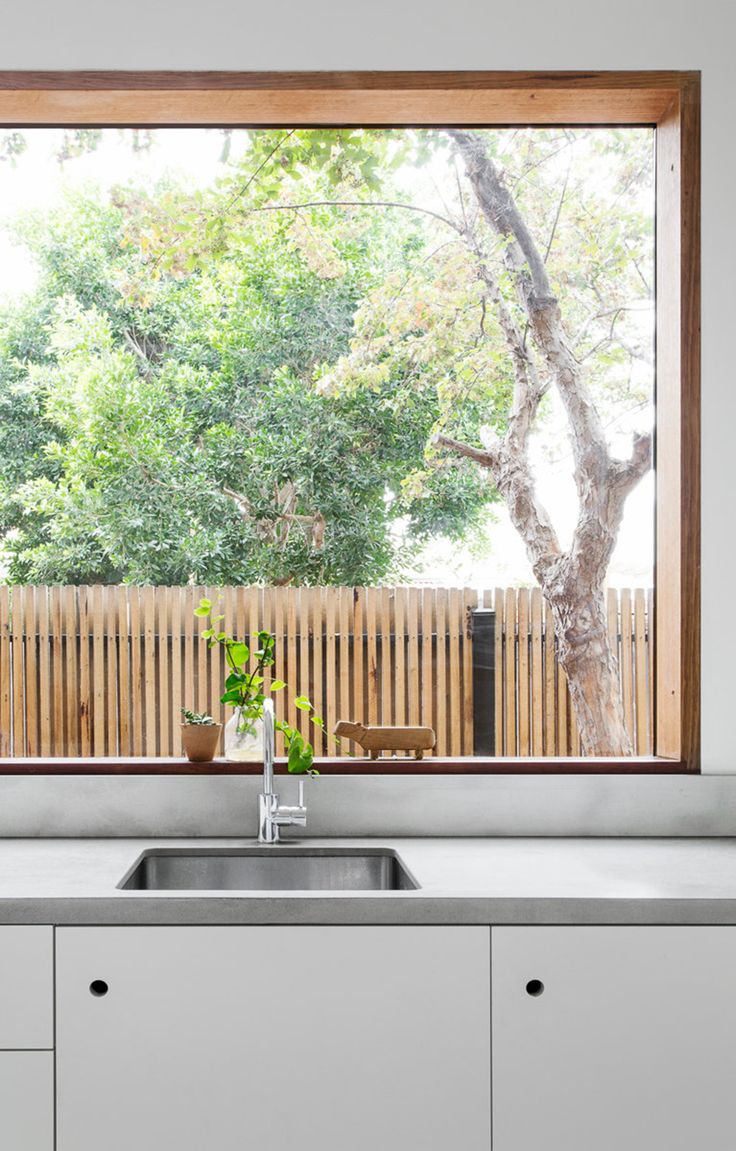 a kitchen sink under a large window next to a wooden fence with trees in the background